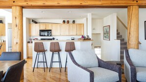 Une cuisine moderne avec des meubles en bois, un îlot central doté de tabourets, et un coin repas avec une table et des chaises.