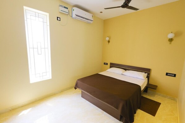 A hotel room with a bed, air conditioning units, a ceiling fan, and a window. - Hazee Beach Stay (Tirukalukundram)