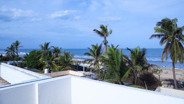 A beach view with palm trees and a clear sky. - Hazee Beach Stay (Tirukalukundram)