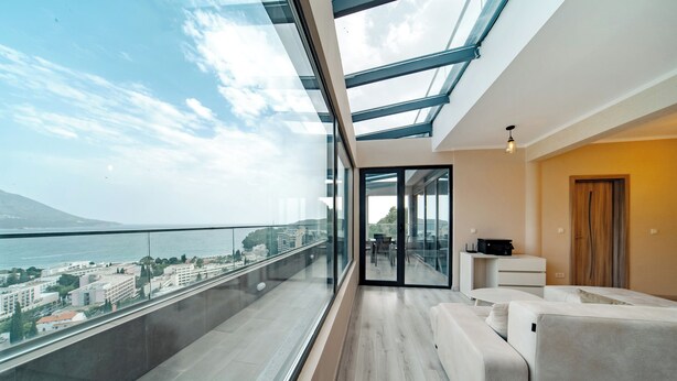 Ein modernes Wohnzimmer mit einem Glasbalkon und Blick auf eine Skyline sowie das Meer.