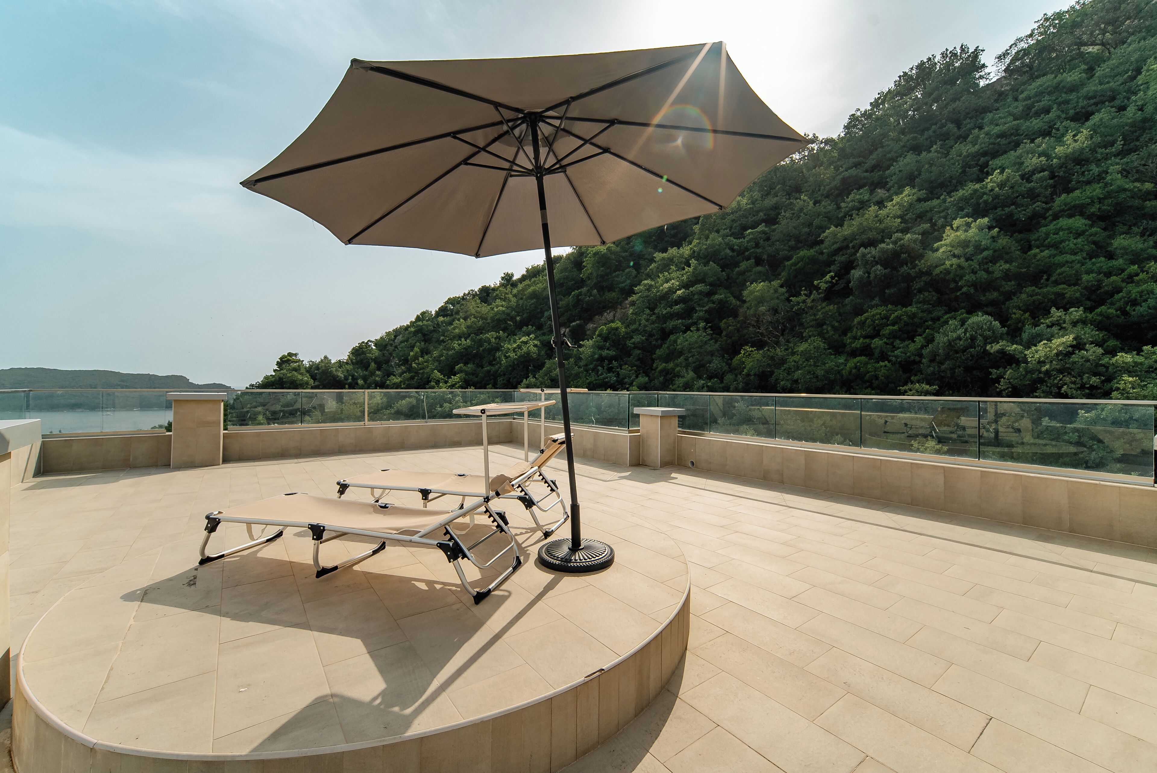 A rooftop terrace with a large umbrella, a metal table, and a view of a forested hillside.