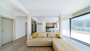 Ein modernes Wohnzimmer mit einer großen, beigefarbenen Eckcouch, Holzboden und Blick auf eine Stadtlandschaft durch große Fenster.