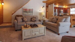 Ein gemütliches Wohnzimmer mit zwei Sofas, einem Couchtisch und einem Bild an der Wand. Im Hintergrund ist eine Küche zu sehen.
