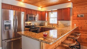 Eine moderne Küche mit Holzschränken, Edelstahlgeräten, Granit Arbeitsplatten und einer Bar.