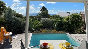 Zona de piscina con una mesa dispuesta para dos personas, rodeada de vegetación exuberante y vistas al océano.