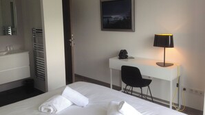 Habitación de hotel con cama, escritorio, silla, lámpara de escritorio, un cuadro en la pared y una toalla sobre la cama.