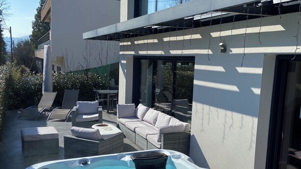 Un espacio exterior moderno con jacuzzi, mobiliario de exterior y vistas a un edificio con grandes ventanales.