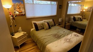 A bedroom with a large bed, a nightstand, a mirror, a window with blinds, and a wall-mounted Buddha statue.