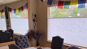 A dining area with a round table, four chairs, a ceiling fan, and a window with blinds.