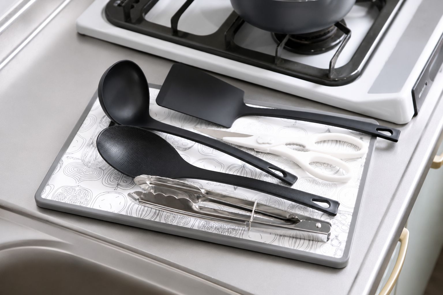 A kitchen counter with a stove, a sink, and various utensils including a spatula, spoon, tongs, and a grater.