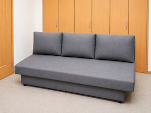 Un canapé gris, de faible hauteur et au design épuré, placé devant une armoire en bois dotée de deux poignées apparentes.