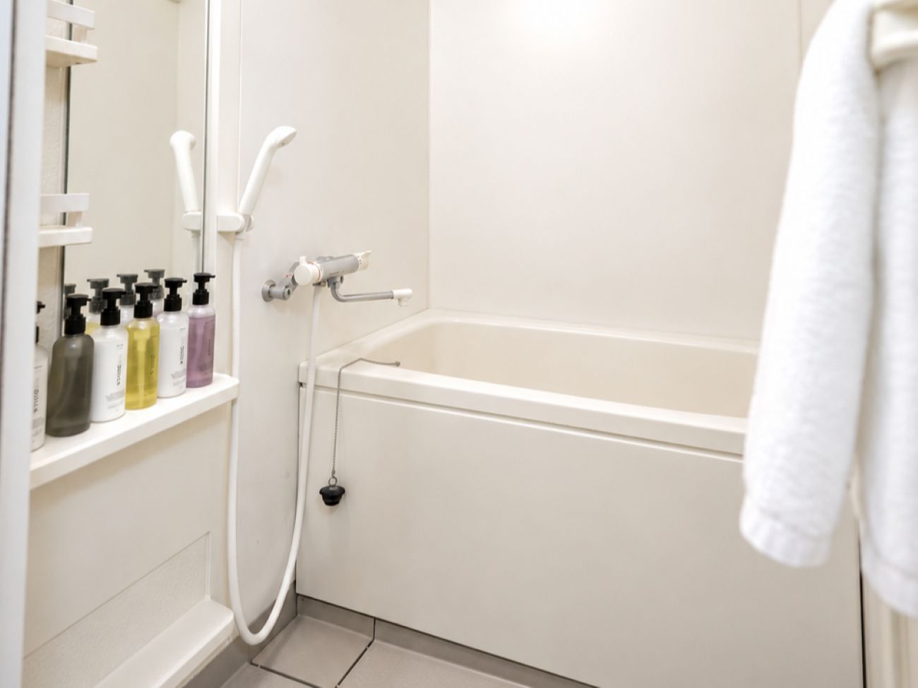 A bathroom with a bathtub, a shower, and a shelf with toiletries.