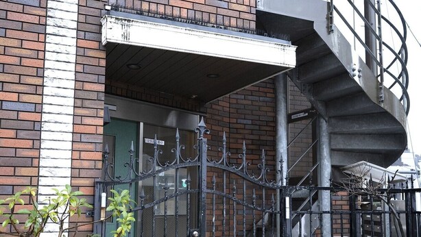 Un bâtiment en briques doté d’un escalier en colimaçon, d’une entrée fermée par un portail et de plantes en pot.