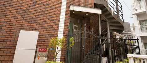A brick building with a staircase leading to an upper floor, a gated entrance, and potted plants.