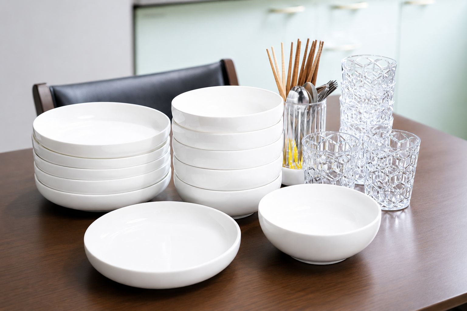 A dining table with stacked white plates, a glass vase with chopsticks, and clear glassware.