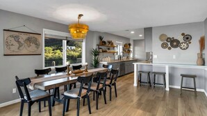 A modern kitchen with a dining area, featuring a large wooden table, black chairs, and a hanging light fixture. - Horizon Haven•Hot Tub•Views•Game Room•Speakeasy (Tucson)