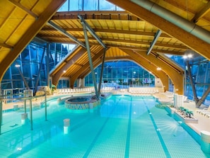 Ein Innenpool mit Holzbalkenüberdachung und großen Glaswänden.