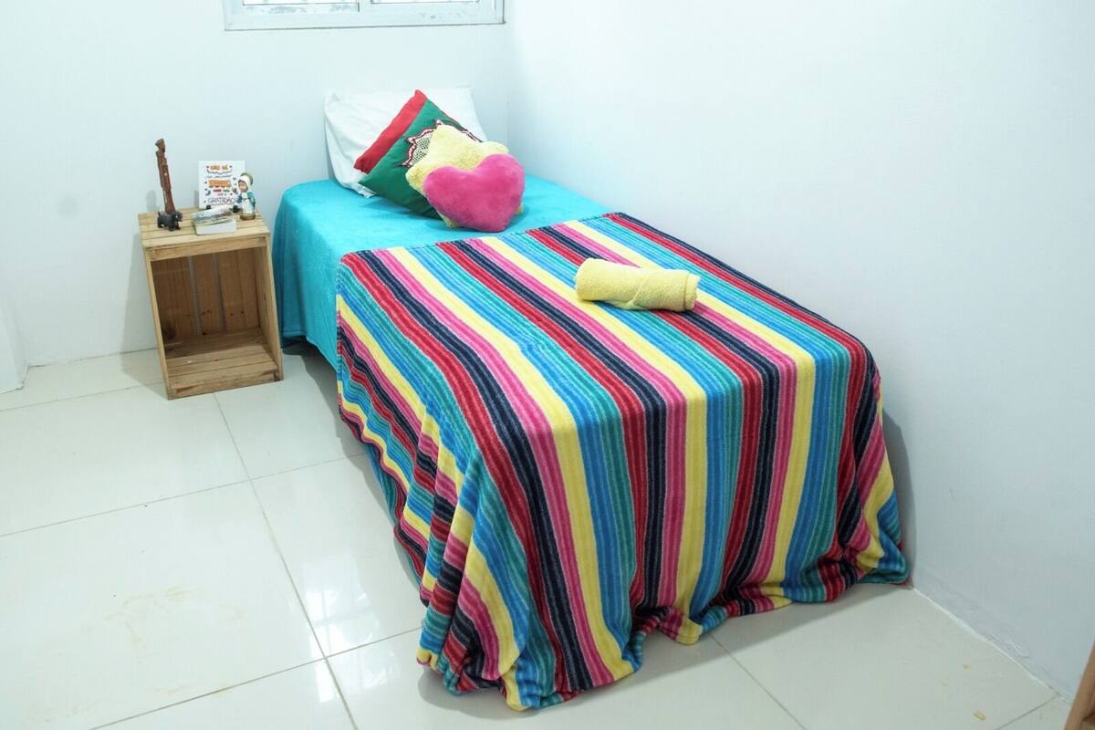 Una stanza piccola e colorata, con un letto, un comodino e una finestra.