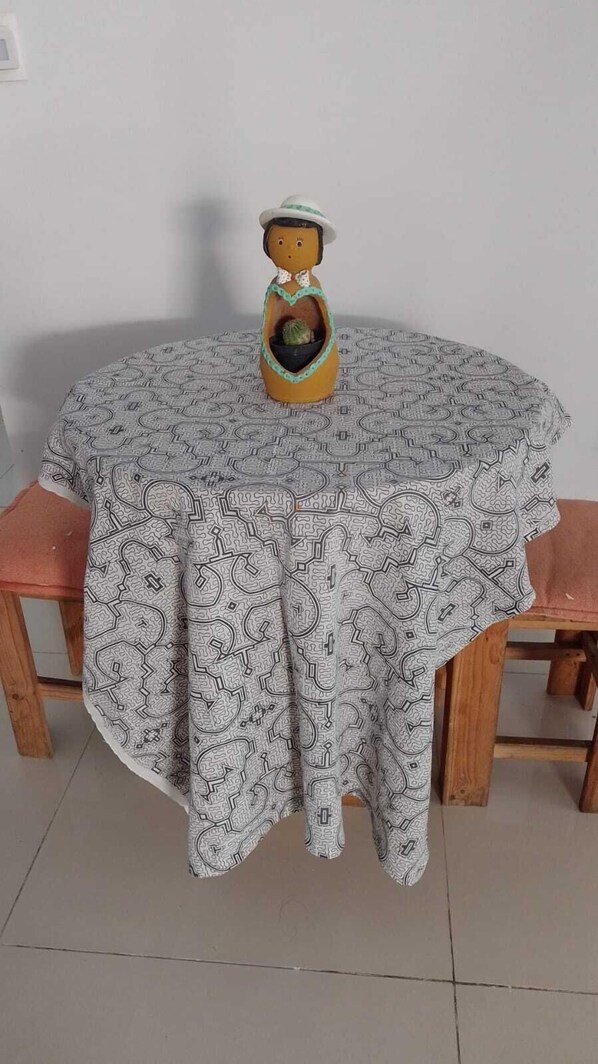 A round table with a patterned tablecloth, two wooden chairs, and a decorative ceramic figure on the table.