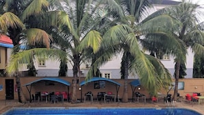 A swimming pool with palm trees and outdoor seating areas. - Tavern Luxury Hotel and Suites Ltd (Kaduna)