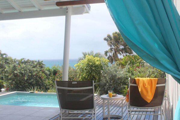 A poolside area with two chairs and a table, overlooking a pool and a view of the ocean.