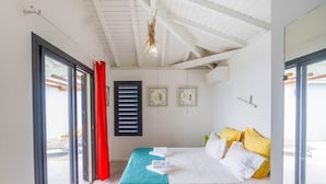 Une chambre d’hôtel avec un lit, une fenêtre avec des stores, un rideau rouge et un ventilateur de plafond.