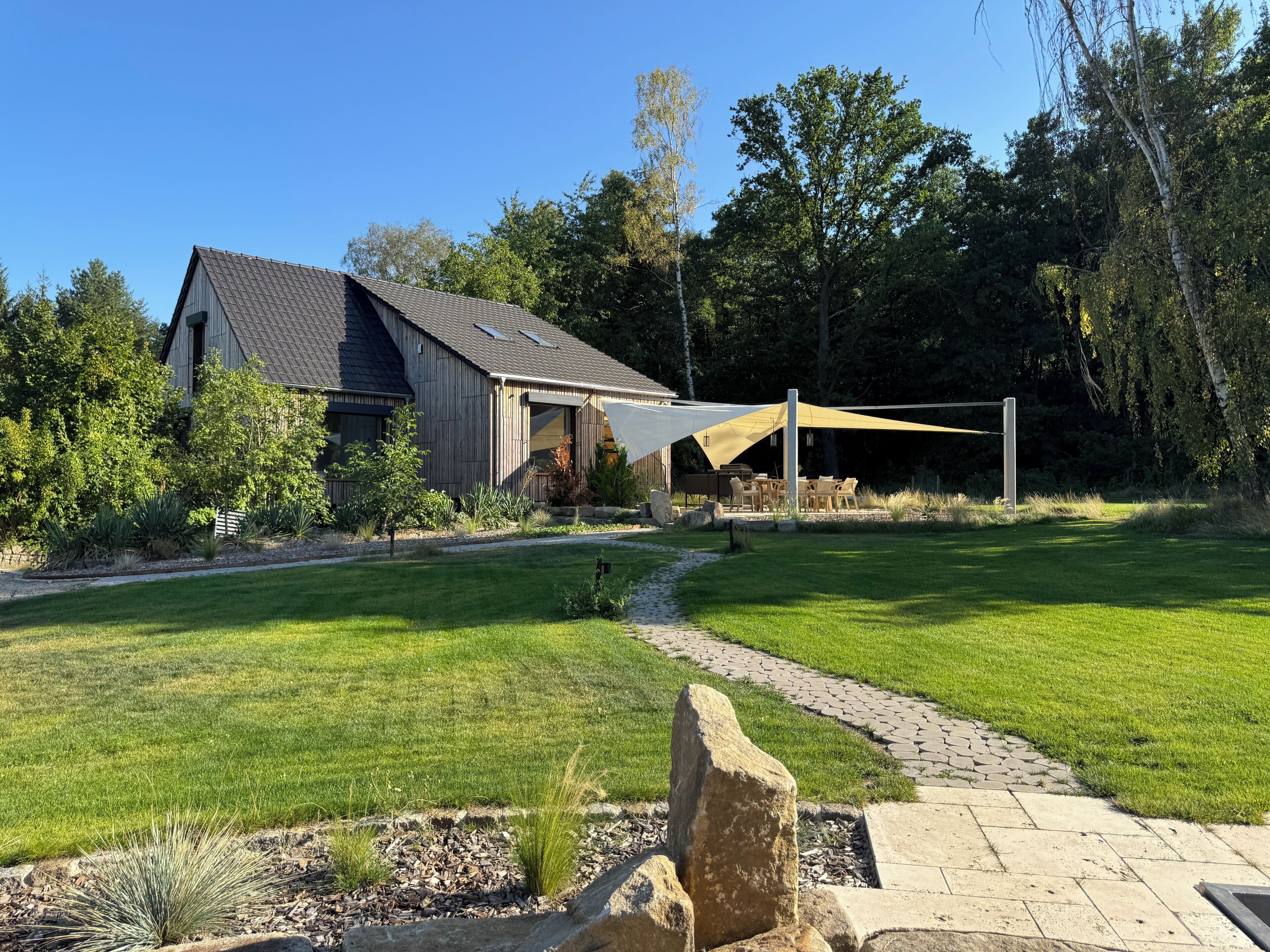 A house with a covered patio, a paved walkway, and a well-maintained lawn.