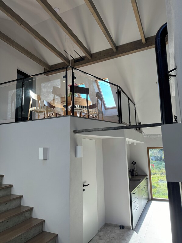 A modern interior with a staircase leading to a loft area, a kitchen with a view, and a dining area with a glass railing.