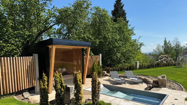 Un área de piscina exterior moderna con sillones de descanso, una pérgola de madera y un sendero de piedra.