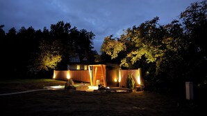 Una casa moderna con terraza de madera, piscina y jardín iluminado al atardecer.
