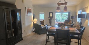 A dining area with a dark wood table, chairs, and a cabinet. There is a window with blinds, a lamp, and a plant.