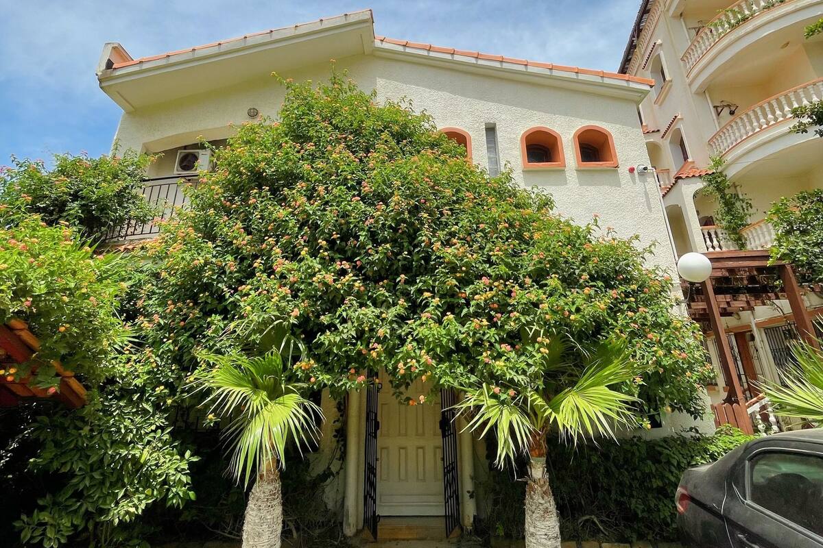 A multi-story building with a white facade, a red-tiled roof, and a balcony with a railing.