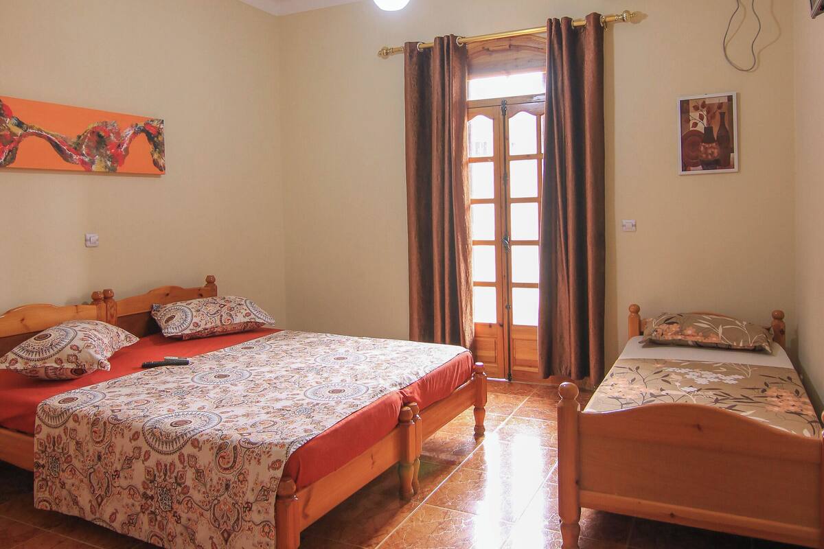A room with two beds, a ceiling fan, a window with curtains, and an air conditioning unit.