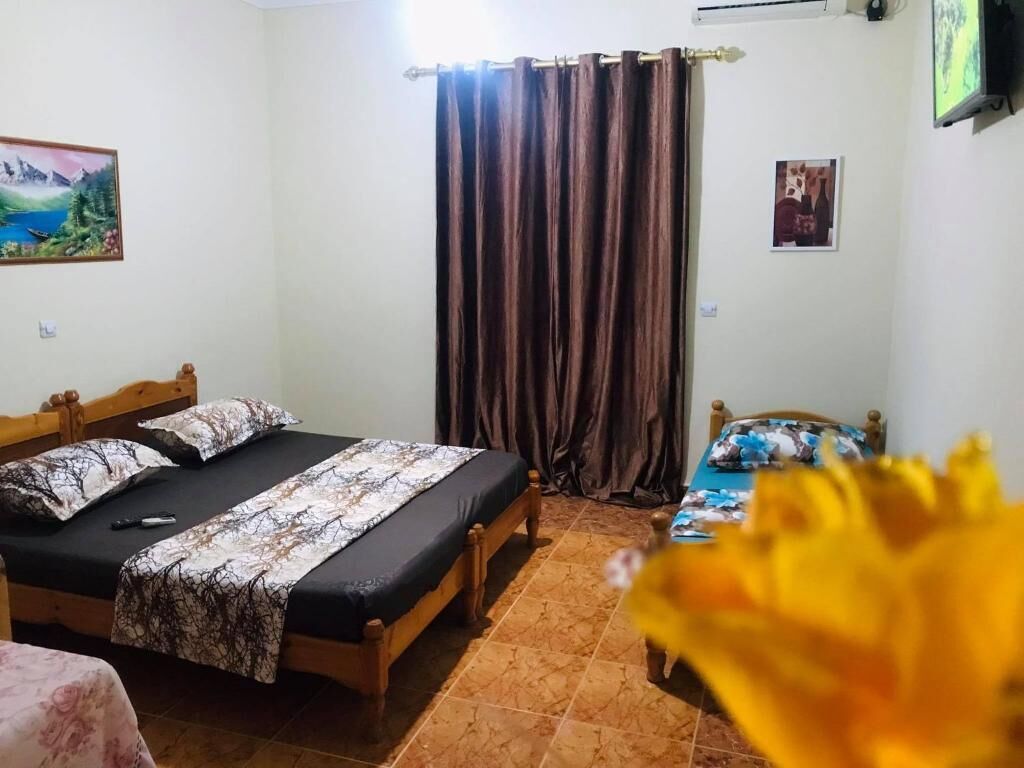 Un dormitorio con cama de madera, mesita de noche, una pequeña mesa, una cortina y un cuadro en la pared.
