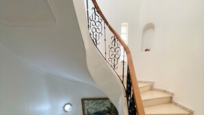 Un escalier en colimaçon, doté d’une rampe en bois et de balustrades en métal noir, mène à un palier où se trouvent un tableau et une petite alcôve.