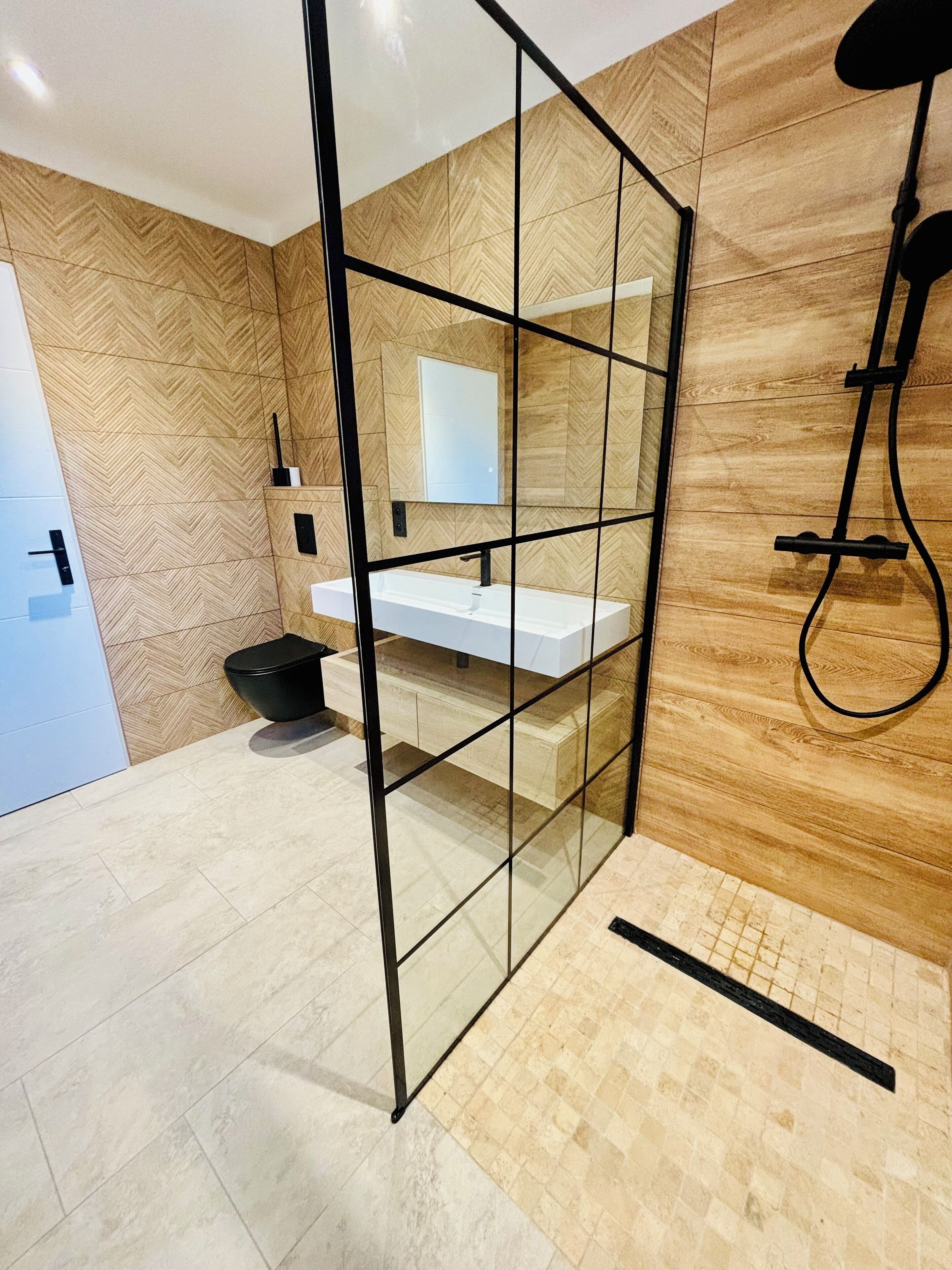 Un baño moderno con un patrón de pared de madera en espiga, un lavamanos blanco y un box de ducha de vidrio.