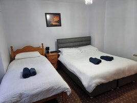 Una habitación de hotel con dos camas individuales, una mesita de noche con lámpara, un cuadro en la pared y un candelabro.