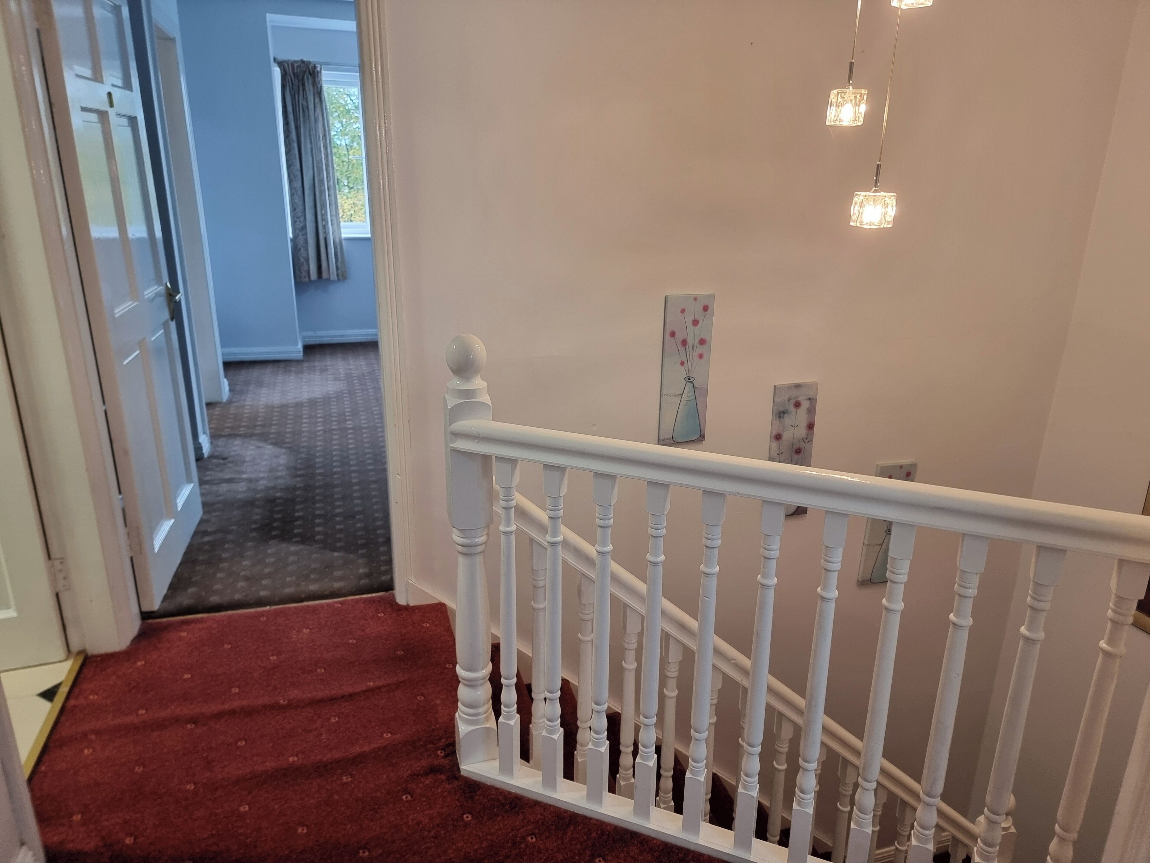 Un escalier avec des balustrades blanches et une moquette rouge menant à une pièce dotée d’une porte et d’une fenêtre avec des rideaux.
