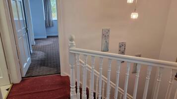 Eine Treppe mit weißen Balustraden und einem roten Teppich, der zu einem Raum mit einer Tür und einem fensterartigen Öffnungsstück mit Vorhängen führt.