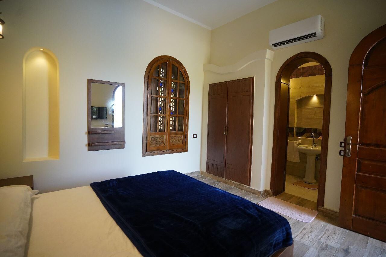 Un dormitorio con cama, espejo, armario y un arco que da acceso a un baño.