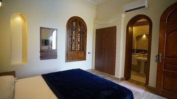 Un dormitorio con cama, espejo, armario y un arco que da acceso a un baño.