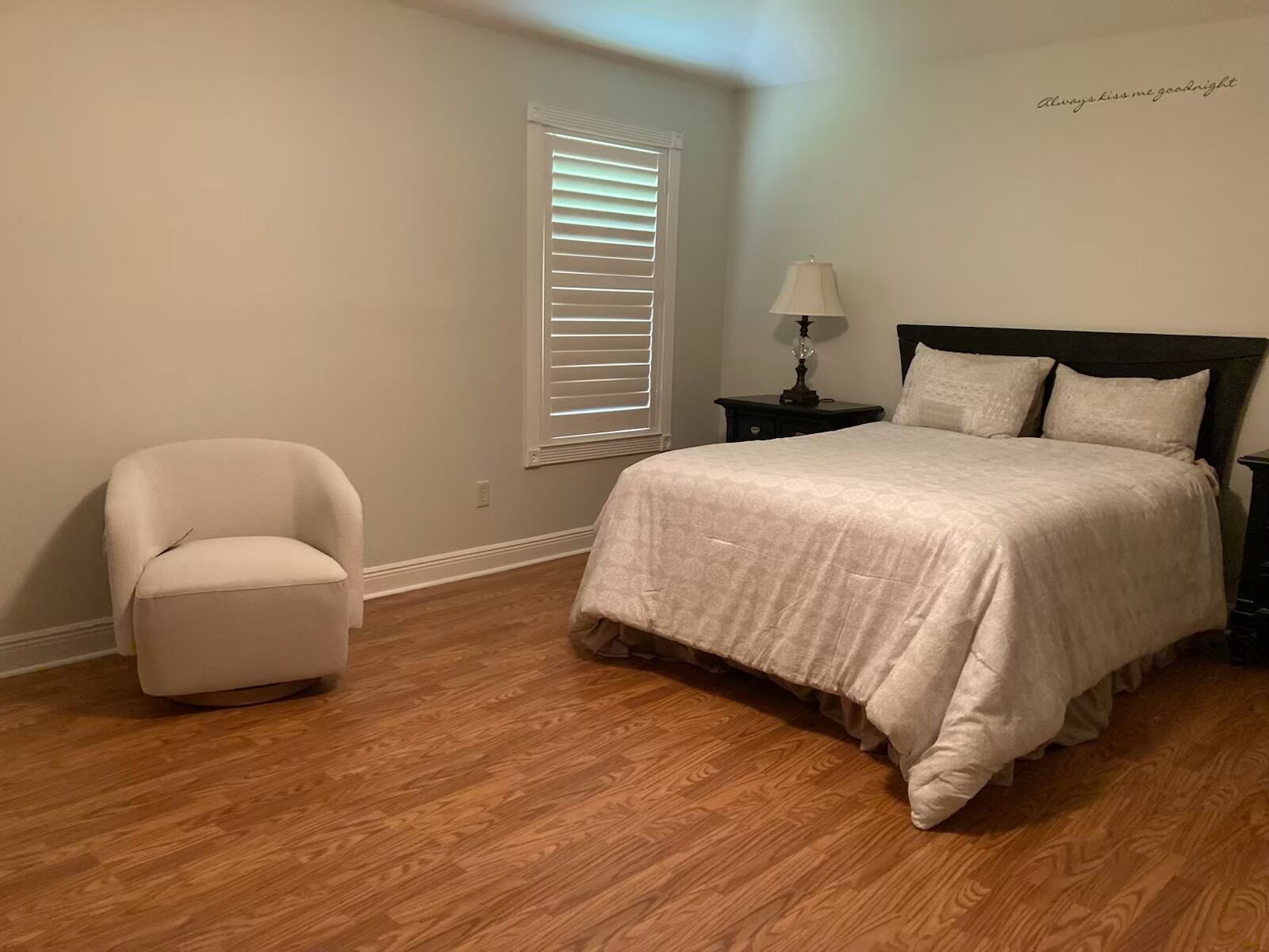 A bedroom with a bed, a chair, a nightstand, a lamp, and a window with blinds.