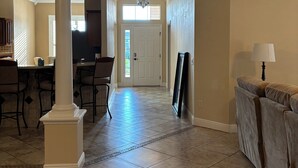 A spacious living area with a high ceiling, a dining area with chairs and a table, and a sofa with a lamp. - Upgraded 3:2 House in Amelia mins to Sumter Landing, golf & pool. New rental. (The Villages)