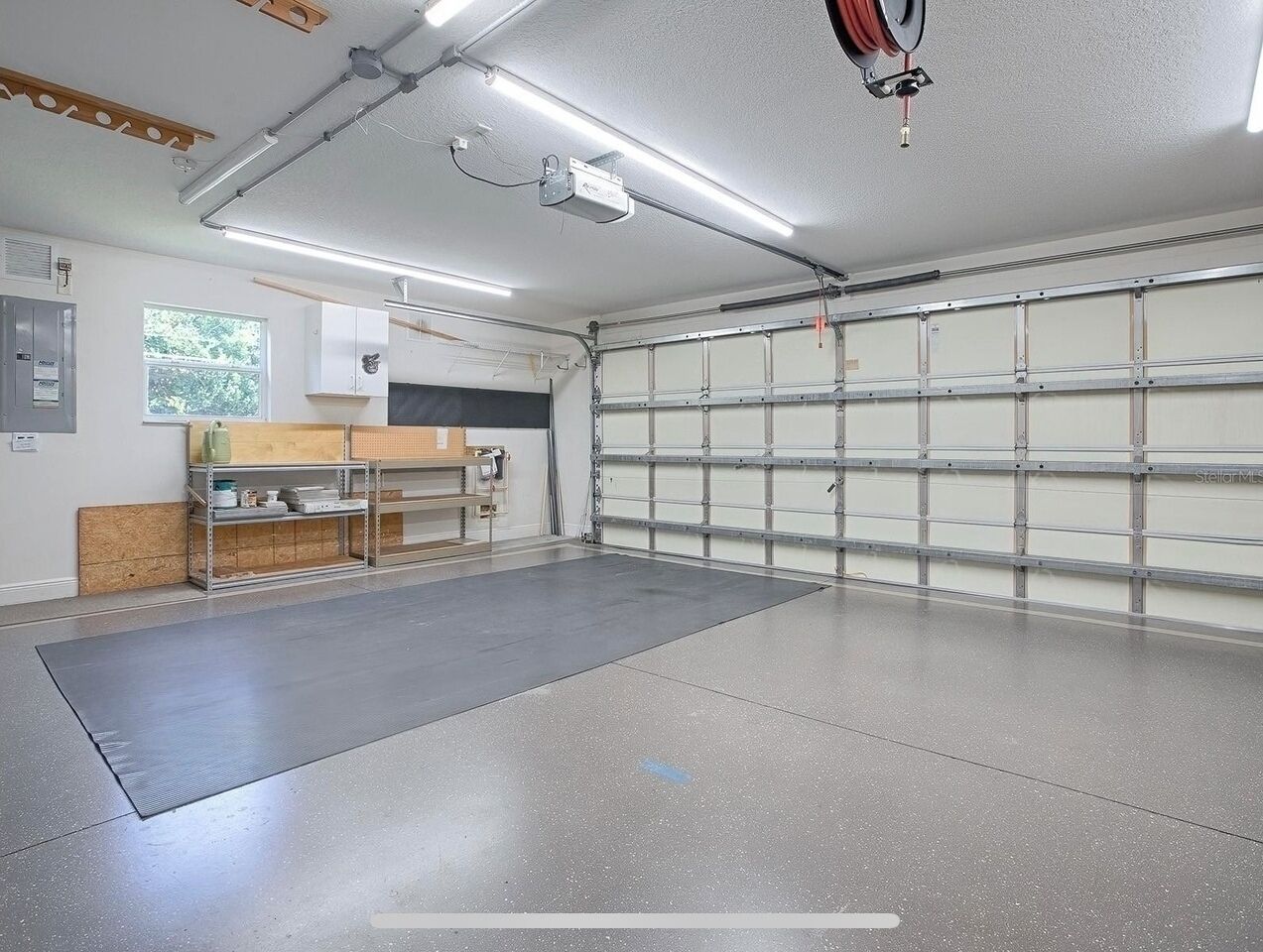 Een schone, goed verlichte garage met een ruime werkbank en een plankensysteem, een garage deur en een betonnen vloer.