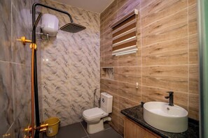 A bathroom with a marble wall, a wooden vanity, a white sink, and a shower with a handheld showerhead. - Grand Dream Hotel  (Abuja)