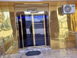 A reception area with a glass door, a sign above it, and an air conditioning unit to the right. - Grand Dream Hotel  (Abuja)