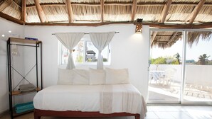 A bedroom with a bed, a shelf, a window with curtains, and a view of the outside. - Charming rooftop bungalow 1 block from the beach! (Corral del Risco)