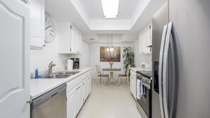 A modern kitchen with white cabinetry, a dishwasher, a refrigerator, and a dining area with a table and chairs. - CASA FAMILIA - 1st floor 2-bedroom unit (Phoenix)