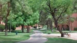 A pathway through a landscaped area with trees and a building in the background. - CASA FAMILIA - 1st floor 2-bedroom unit (Phoenix)