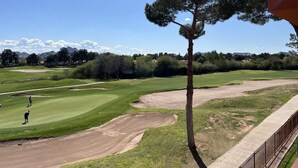 Un campo da golf con cielo sereno, un albero solitario e una catena montuosa in lontananza.
